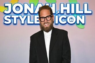 Jonah Hill smiling on a red carpet wearing a sleek suit, celebrating his recent career and personal life milestones.