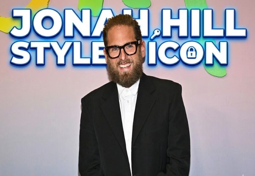 Jonah Hill smiling on a red carpet wearing a sleek suit, celebrating his recent career and personal life milestones.