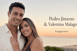 A romantic evening proposal setup on a white sand beach featuring a large heart-shaped arch constructed from hundreds of red roses, illuminated by a neon sign that reads 'Will You Marry Me?' surrounded by glowing candles.