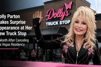 Dolly Parton smiling while cutting a ribbon with large bedazzled pink scissors in front of her new Tennesseean travel stop.